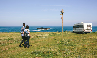 Young couple taking a walk near the coast with a camper in the background