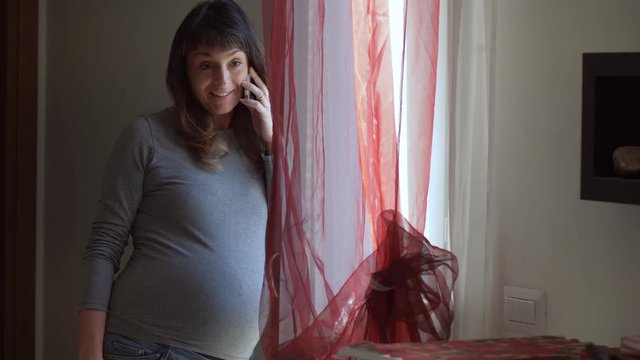 smiling and happy young pregnant woman talking on the phone - indoor