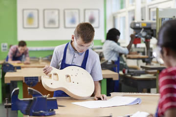 Male High School Student Building Guitar In Woodwork Lesson