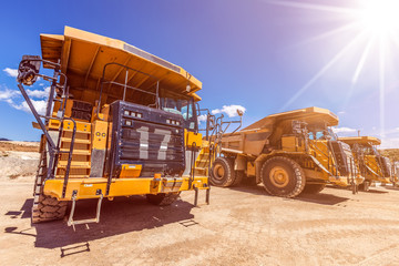 Row of large dumper trucks on construction site with sun flare