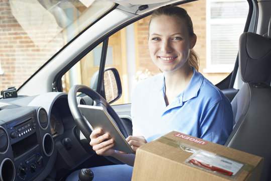 Portrait Of Female Courier In Van With Digital Tablet Delivering Package To Domestic House