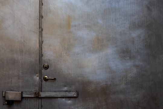 Closeup of closed scratched grungy shiny steel door with locks and handle.