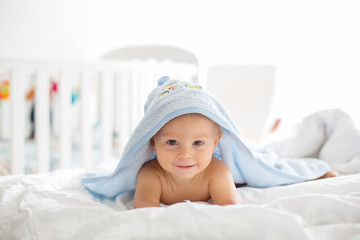 Little cute baby boy, lying in bed with towel after bath, sunny bedroom