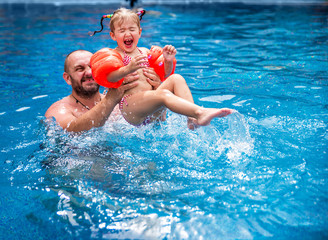 Dad teaches a little daughter to swim in the pool.