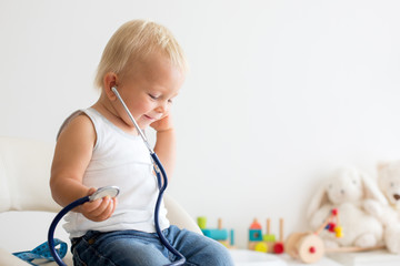 Sweet child, baby boy, playing doctor using stethoscope to listenhis hearth beat