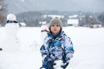 Fototapeta na wymiar Family with children, building snowman in the park in little village in Austria