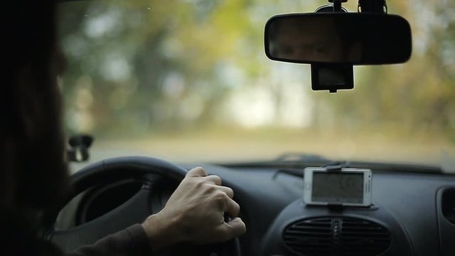 A man gets into the car and turns on the navigator on the smartphone, soft focus