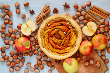 Autumn tart on the wooden board decorated with fresh apples, hazelnuts and spices - anise stars and cinnamon on the gray kitchen background. Thanksgiving pie with raw ingredients. Top view
