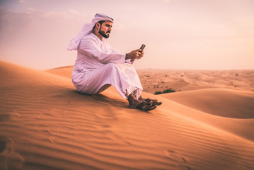 Naklejka premium Arabski mężczyzna chodzący po pustyni z tradycyjnymi ubraniami emiratów