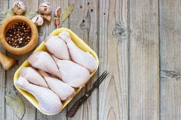 Bowl with raw chicken legs on wooden background, top view