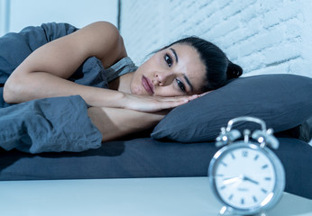 Attractive woman staring at alarm clock trying to sleep feeling stressed depressed and sleepless