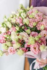 beautiful spring bouquet. Young girl holding a flowers arrangement with lisianthus of pink colors. white wall.