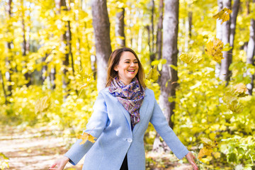 Autumn, nature and fun concept - Young beautiful woman in blue coat throwing bouquet of leaves