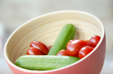 Liitle tomatoes with little cucumbers in a wooden bowl with soft colors