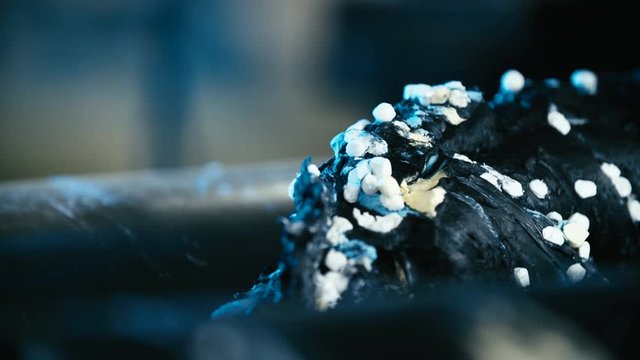 Mixing rubber with chemical ingredients 4K. Long shot of mixed rubber mass in focus while being rolled into cylinder machine. Industrial rubber production line.