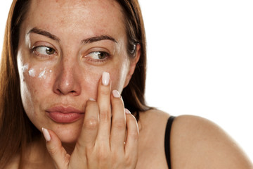 beautiful middle-aged woman applying moisturizer on her face on white background © vladimirfloyd