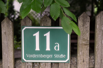 Gartenzaun daran ein Straßennamen und Hausnummerschild befestigt