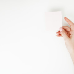 Fototapeta premium Flat lay, top view. Beauty and fashion concept. Beautiful female hands with red manicure. Minimal style. Minimalist photography. Pale composition with girl's hand holding card on white background