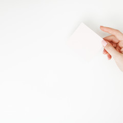 Flat lay, top view. Beauty and fashion concept. Beautiful female hands with red manicure. Minimal style. Minimalist photography. Pale composition with girl's hand holding card on white background