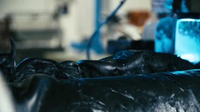 Mixing rubber mass between spinning cylinders close-up 4K. Long shot dolly slide of mixed rubber mass in focus while being rolled into cylinder machine. Industrial rubber production line.