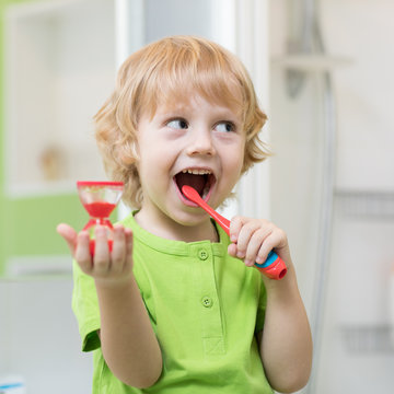 Little boy brushes his teeth monitoring lasting with hourglass