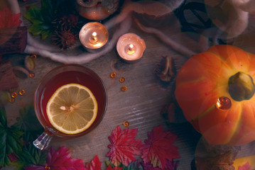 Autumn hot tea with lemon and spices in glass cup.on rustic table with leaves and pumpkins. Autumn Halloween style.