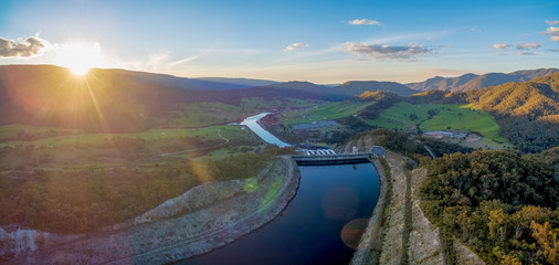 Wide aerial panorama of Tumut river and mountains at sunset with sun flare. NSW, Australia