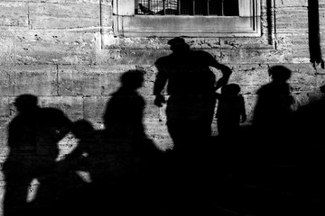 Shadows of the people on a real stone wall at The New Mosque at Istanbul. Some people are sitting and walking and a father is holding his kids hand.