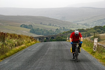 Cyclist pedals on after getting to the top of a very steep hill in the Yorkshire Dales National Park, UK