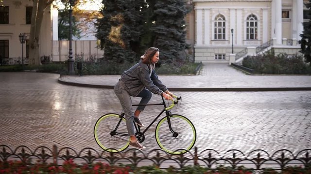 Woman riding bike on city paved road. Woman bicycle rider have a ride in the morning. Empty city street with a beautiful old buidings on the background