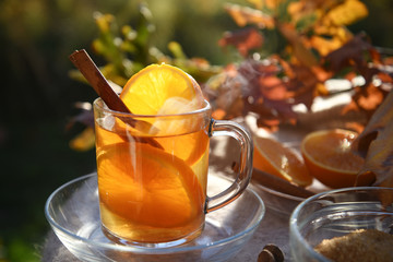 hot tea drink with orange slices and cinnamon in a glass cup in backlit in the autumn garden,...