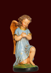 Angel in prayer with blue dress, gypsum, statue made of gypsum and hand painted, isolated on dark red background