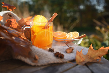 hot tea with orange slices and cinnamon on a wooden garden table with a blanket and autumn leaves,...