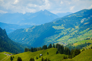 Fototapeta na wymiar Summer landscape of green hills an mountain village in Switzerland