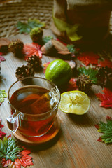 Autumn hot tea with lemon and spices in glass cup.on rustic table with leaves and pumpkins. Autumn Halloween style.