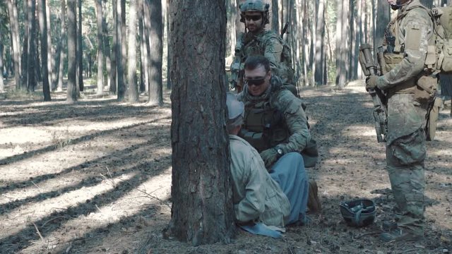Soldiers beating captive man in forest during interrogation