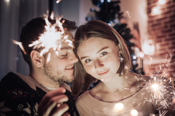 Young couple celebrating Christmas at home. They having fun with sparklers.