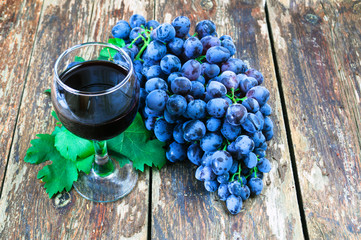 Grapes on a old wooden table and a glass of red wine