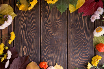 Autumn background. Bright orange berries, very flowers and leaves on a brown wood background. Background for autumn holidays and thanksgiving day.