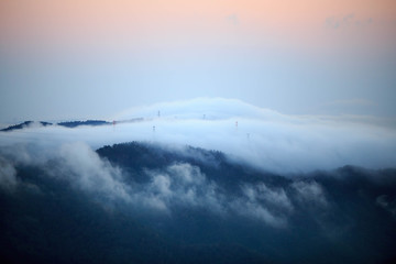 Obraz premium Electrical towers peak out from morning fog as sky glows orange with first signs of sunrise