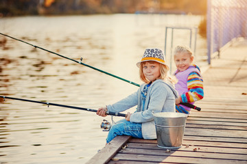 Little girls fishing on the lake, sitting on a wooden pontoon