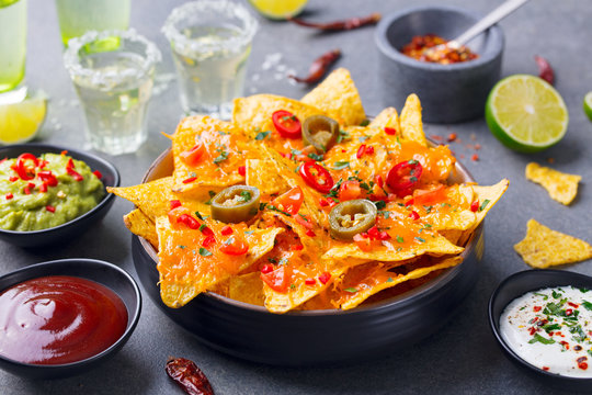 Nachos chips with melted cheese and dips variety in black bowl. Grey stone background. Close up.
