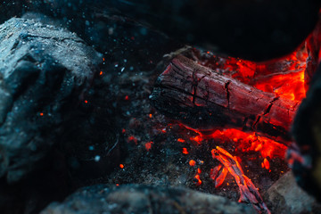 Smoldered logs burned in vivid fire close up. Atmospheric background with orange flame of campfire. Unimaginable detailed image of bonfire from inside with copy space. Smoke and glowing embers in air.