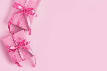 Box wrapped in pink gift paper and ribbon, on a pink background. Copy space, rose design shading.
