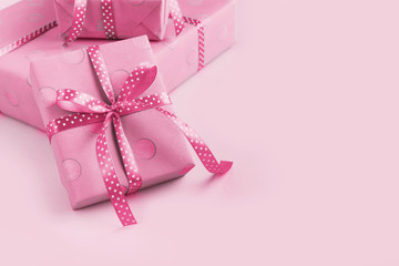 Box wrapped in pink gift paper and ribbon, on a pink background. Copy space, rose design shading.
