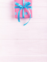 A gift wrapped in pink paper in a blue circle and ribbon, on a white wooden table. Copy space, rose design shading.
