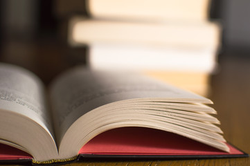 Closeup of open book with stack of books in the background