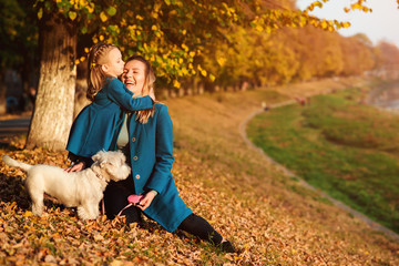Mother and daughter on autumn walk with dog. Happy loving family having fun. Small white dog and family enjoying together outdoors. Family, pet and lifestyle concept.
