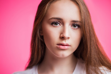 Naklejka premium Horizontal close-up portrait of beautiful young girl on pink background. A woman looks at the camera with a piercing gaze