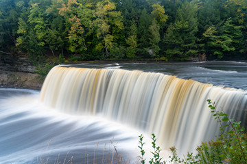 Tannin stained rushing water of Tahquamenon River rushing over the sandstone falls in early autumn as the foliage is just starting to change in the Upper Peninsula, Michigan